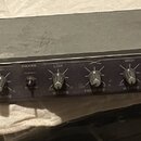 Černý rackový přístroj s nápisem 2 WAY STEREO CROSSOVER a logem AUDIOMAX. Na předním panelu se nachází šest otočných ovířkovaných potenciometrů s pop…