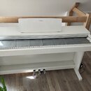 Bílé digitální piano s doprovodným stojanem a šedým krytem klávesnice. Na horní části je viditelné logo YAMAHA a stejný nápis se nachází v pravém dol…
