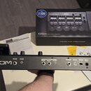 Černý efektový procesor s nápisem ZOOM na levé straně. Na zadním panelu jsou viditelné vstupy a výstupy s popisky INPUT, AUX IN, OUTPUT (L/MONO, R),…