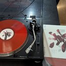 Černý gramofon Pioneer DJ PLX-500 s červeným vinylovým diskem. Na přístroji je vidět nápis Pioneer DJ a DIRECT DRIVE TURNTABLE PLX-500. Vedle gramofo…