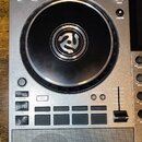 Šedý DJ controller značky Numark s velkým černým jog-wheelem. Na ovládacím panelu jsou viditelné nápisy MIX, VOLUME, FILTER, LIGHTING, SYNC, SYNC OFF…