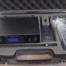 Černý kufr s pěnovou výplní obsahuje vysílač a přijímač in-ear monitoringu. Na vysílači je nápis „the t.bone IEM100T UHF STEREO TRANSMITTER“ a na při…