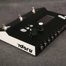 Černý elektronický přístroj s bílými bočními stěnami. Na horní straně jsou tři kovové přepínače, čtyři ovládací tlačítka, dva otočné knoflíky a malý…