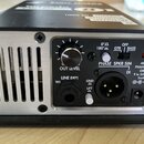 Zadní strana černého elektronického zařízení s hliníkovým předním panelem a ventilačními otvory. Na panelu jsou nápisy OUT LEVEL, LINE (DRY) TRS, PHA…