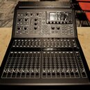 Černý digitální mixážní pult s displejem a několika řadami posuvníků. Na horním panelu jsou umístěny různé ovládací knofíky, tlačítka a digitální dis…