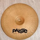 Zlatý kovový činel s povrchem pokrytým drobnými hámrkovanými důlky. Na spodní části je černý nápis PAiste a pod ním menší text MADE IN SWITZERLAND. P…