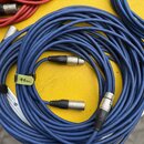 Modré audio kabely s konektory typu XLR. Na dvou z nich jsou černé stahovací pásky s nečitelným žlutým nápisem. V levém horním rohu jsou vidět části…