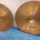 Dvě mosazné činely značky Paiste. Menší z nich má v centru nápis 22", větší má v centru nápis 24". Povrchy jsou s viditelným broušením a mírnými stop…