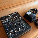 Černý mixovací pult s nápisem 402VLZ4 a logem Mackie. Zařízení obsahuje různé vstupy, potenciometry a přepínače s bílými a modrými popisky. Vedle mix…
