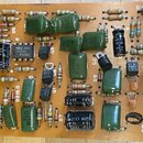 Fotografie zachycuje detail hnědé tiskované desky s elektronickými součástkami, jako jsou rezistory, kondenzátory a tranzistory. Na desce jsou vidite…