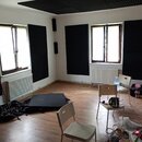 Interiér místnosti s laminátovou podlahou a bílými stěnami. Stěny i strop jsou částečně pokryty černými akustickými panely s vlnitým povrchem. V míst…