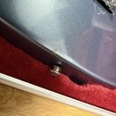 Detailní záběr na modré kovové tělo elektrického nástroje s lesklým povrchem. Na hraně je vidět malý odřep v laku a vyčnívající kovový šroub s podlož…