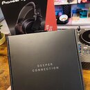 Na fotografii jsou dvě černé krabice. V horní části je vidět obal sluchátek s nápisy Pioneer DJ a HDJ-X5. V popředí drží ruka černou čtvercovou krabi…
