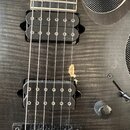 Detail těla černé elektrické kytary s dvěma humbuckery. Na povrchu laku je viditelný výrazný odřap s odsálením materiálu mezi snímači. V dolní části…