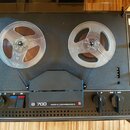 Černý cívkový magnetofon s dvěma průhlednými cívkami. Na předním panelu je bílý nápis B 700 MADE IN CZECHOSLOVAKIA a červené kulaté logo. Přístroj ob…