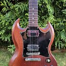 Elektrická kytara s hnědým dřevěným povrchem a černým pickguardem. Nástroj má dva humbuckery, čtyři ovládací knoflíky a přepínač s nápisy RHYTHM a TR…