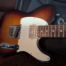 Elektrická kytara s tělem v provedení sunburst a bílým pickguardem. Na hředníku jsou dva oválné ovládací knofíky a kovový kryt s pickupem. Hmatník je…