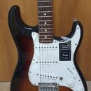 Elektrická kytara s tłem v barvě sunburst a bílým pickguardem. Na těle je nalepený štítek s nápisy PLAYER SERIES STRATOCASTER a logo Fender. Nástroj…