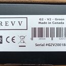 Fotografie detailu bílé nálepky na kartónovém obalu. Na nálepce je uveden nápis REVV, označení G2 - V2 - Green a Made in Canada. Je zde vidět logo CE…