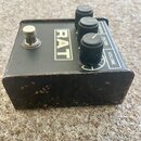 Černý kytarový efekt s nápisem RAT. Na horní straně jsou tři černé oválové knoflíky s popisky DISTORTION, FILTER a VOLUME. Přístroj vykazuje výrazné…