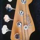 Hlava čtyřstrunné basové kytary z přírodního dřeva v černém kufru. Na hlavě je vidět logo Fender a nápis PRECISION BASS, pod kterým je drobný nečitel…