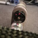 Detailní pohled na spodní část stříbrného mikrofonu s připojeným konektorem. Uvnitř černého plastového objímky je vidět kovový kontakt s několika čer…