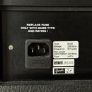 Detail zadní strany černého hudebního zařízení s napájecím konektorem. Nad konektorem je bílý nápis REPLACE FUSE ONLY WITH SAME TYPE AND RATING ! Ved…