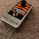 Stříbrný kytarový pedál s oranťovými pruhy na horní straně. Na čelní straně je nápis electro-harmonix a pod ním MADE IN NYC, USA. Na horní části je č…