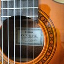 Detail akustické kytary s viditelným hředníkem a otvorem rezonanční skříně. Uvnitř otvoru je nalepený štítek s nápisy YAMAHA, CGX-111SC a textem Made…
