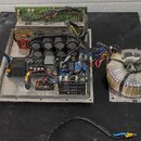 Fotografie zachycuje vnitřek elektronického zařízení, pravděpodobně zesilovače, bez krycího šasi. Je vidět hliníkový základ s instalovanými kondenzát…