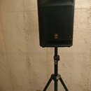Černý reproduktor umístěný na černém stativu. Na přední mřížce je viditelné logo a nápis YAMAHA. Povrch reproduktoru vykazuje mírné opotřebení v podo…