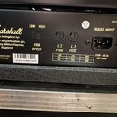 Zadní panel černého zesilovače značky Marshall s nápisem Made in England by: Marshall Amplification plc, Bletchley, Milton Keynes, England. Jsou zde…