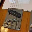 Detail elektrické kytary s dřevěným tělem v žlutohnaté barvě a bílým pickguardem. Je zde vidět černý humbucker snímač a chromovaný kobylník s pěti st…