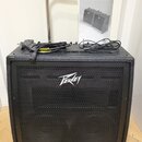 Černý klavírní kombo zesilovač s kovovou mřížkou, na které je bílé logo Peavey. V dolní části je stříbrný nápis KB5. Na horní straně leží napájecí ka…