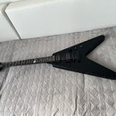 Černá elektrická kytara s tělem ve tvaru V. Na hlavě hрифu je bílý nápis Schecter. Kytara má dva humbuckery, dva ovládací knoflíky a černý hardware.…