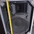 Černý reproduktorový box v hliníkovém rámu s dvěma výstupními otvory. Horní část obsahuje hornový reproduktor a spodní část je kryta kovovou mřížkou.…