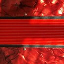 Detail červené harmoniky s výraznou texturou povrchu připomínající mramor. V horní části je nápis MADE IN CZECHOSLOVAKIA a vedle něj nečitelné sériov…