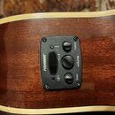 Detailní záběr na černý ovládací panel předzesilovače s nápisem FISHMAN® zabudovaný v hnědém dřevěném těle akustické kytary. Panel obsahuje tři otočn…