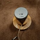 Fotografie zachicuje malý reproduktor s šedým krytem, který je umístěn na dřevěném podstavci. Na horní části reproduktoru je černý nápis 11 12 a pod…