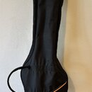 Černý pol pevný pouzdro (gigbag) na kytaru. V horní části je umístěna malá oranžová štítková nálepka s bílým logem. Pouzdro má v dolní části zip s or…