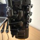 Detailní záběr na černý kovový mechanismus s klapky a písty, pravděpodobně součást saxofonu. Nástroj má černý lakovaný povrch a v dolní části je vidě…