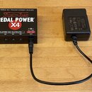 Černý napájecí adaptér Voodoo Lab Pedal Power X4 s nápisem HYBRID DC TRANSFORMER DESIGN. Zařízení má čtyři výstupy označené jako ISOLATED DC OUTPUTS…