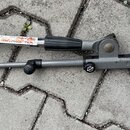 Šedý kovový mikrofonní stojan s chromovaným horním ramenem. Na spojovacím prvku je viditelné kulaté logo s nápisem K&M. Povrch chromovaného dílu vyka…