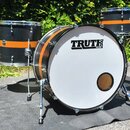 Černá bubnová sada s oranžovými pruhy, která obsahuje basový buben a dva tom-tomy. Na bílém předním zrcadle basového bubnu je černý nápis TRUTH DRUMS…