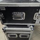 Dvě černé transportní bedny s hliníkovými hranami a kovovými rohy. Horní bedna má v levém horním rohu štítek s nápisem MUSICSTORE professional a na r…