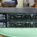 Dvě identické černé rackové jednotky značky dbx s nápisem PROFESSIONAL PRODUCTS A HARMAN INTERNATIONAL. Na zadním panelu jsou vidět vstupy a výstupy,…