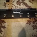 Černý obdélníkový spínací pedál s nápisem Blackstar. Na horní straně se nachází šest kovových tlačítek s bílými popisky: CLEAN, CRUNCH, OVERDRIVE 1,…