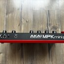 Zadní strana červeného MIDI kontroléru s nápisem AKAI PROFESSIONAL MPKmini play. Jsou zde vidět čtyři černé otočné knoflíky, přepínač POWER (USB/BATT…