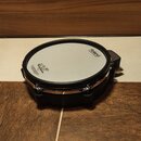 Elektronický buben v černé barvě s bílou pukulní plochou. Na ploše jsou viditelné nápisy Roland a V-Drums. Nástroj má chromovaný obruč s několika šro…