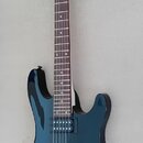 Elektrická kytara s tmavě modrým lakovaným tělem a hnědým hmatníkem. Na hlavě je bílé logo Cort. Nástroj má dva humbuckery, fixační most a dvě ovláda…